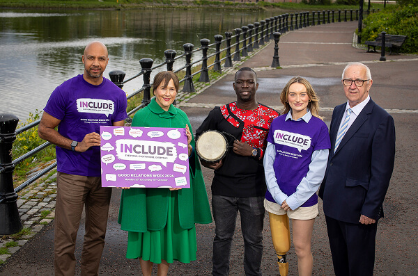 The launch of Good Relations Week 2026 at the waterside, five people holding the Include campaign artwork and a drum.