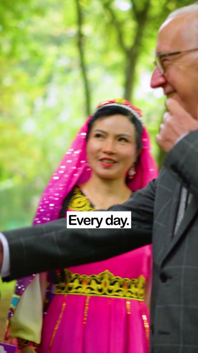 A still from the Good Relations Week film: a woman in a pink headscarf and embroidered dress smiles beside an older man in a check suit, among the trees, with the caption "Every day."